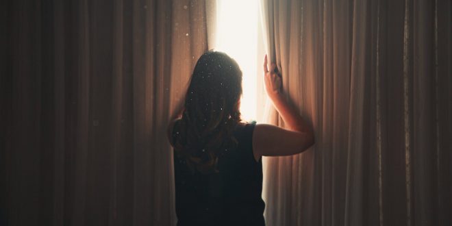 Mental Health during Covid. Unrecognizable woman opening window curtain in shining daylight.